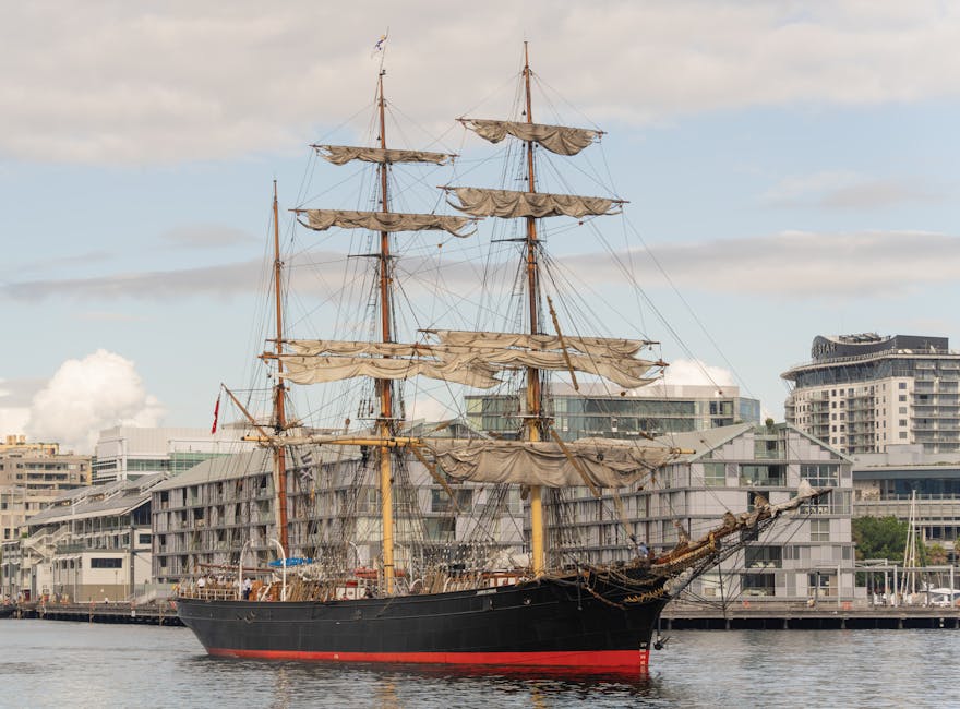 A large, illuminated ship-shaped structure with a glass-domed base is situated outdoors at night. The ship's masts and rigging are made of metal and are lit with yellowish and white lights, creating a